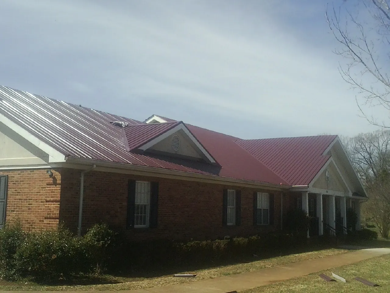 Red metal roof with gabled entries on a long brick building, from a Hail Damage Roof Repair job in Harrisonburg