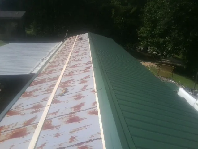 Old rusted panels beside newly installed green metal roofing — Wind Damage Roof Repair by Roofing Brothers in Harrisonburg