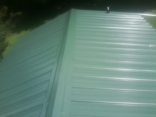 New green metal panels meeting at the ridge of a roof — Flat Roof Repair work by our crew in Harrisonburg