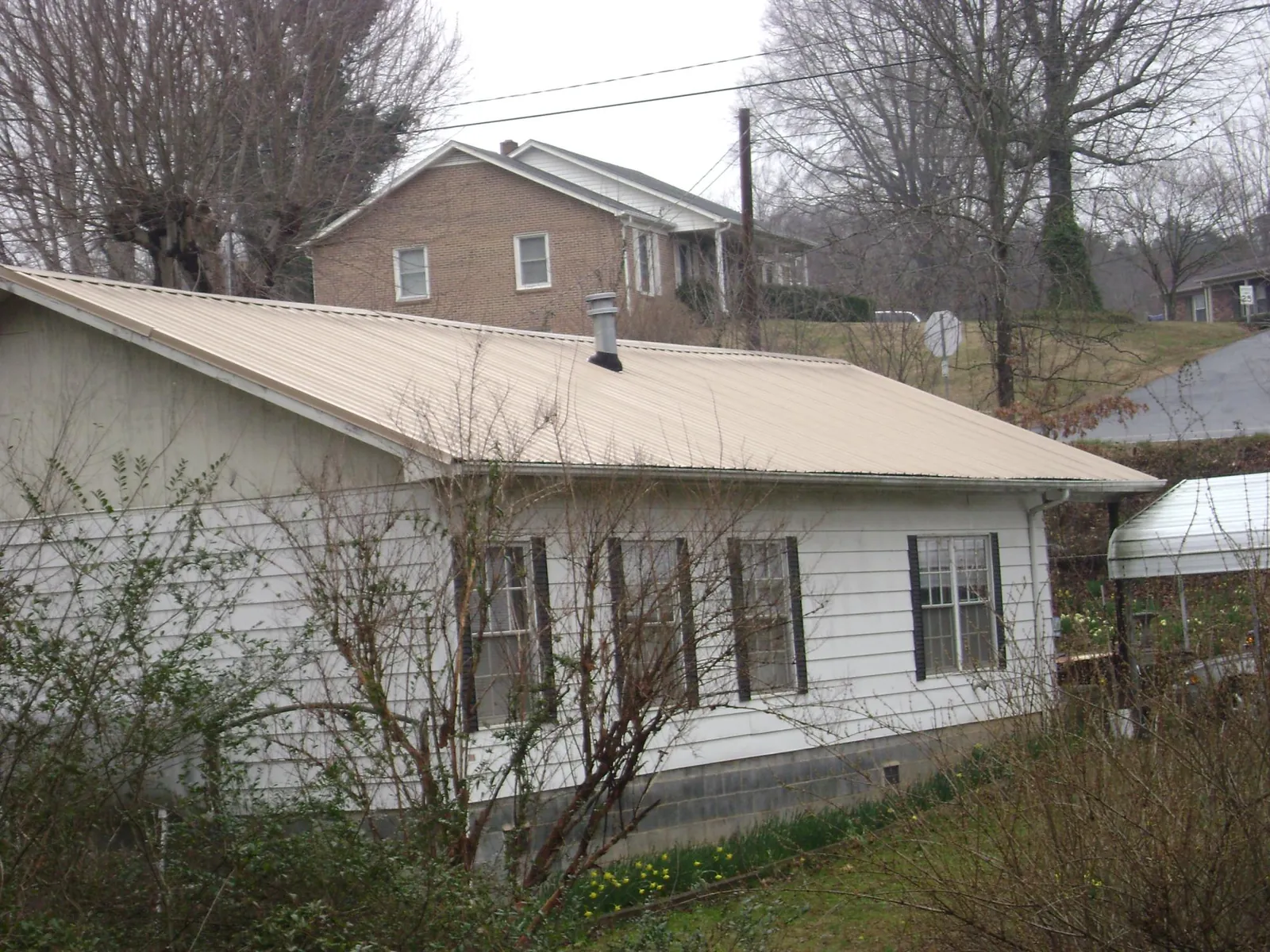Tan metal roof on a white sided house set into a hillside — Commercial Roofing by Roofing Brothers in Harrisonburg